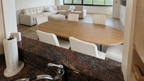 Una cocina moderna con encimeras de granito, un lavamanos de acero inoxidable y una zona de comedor con una mesa de madera y sillas blancas.