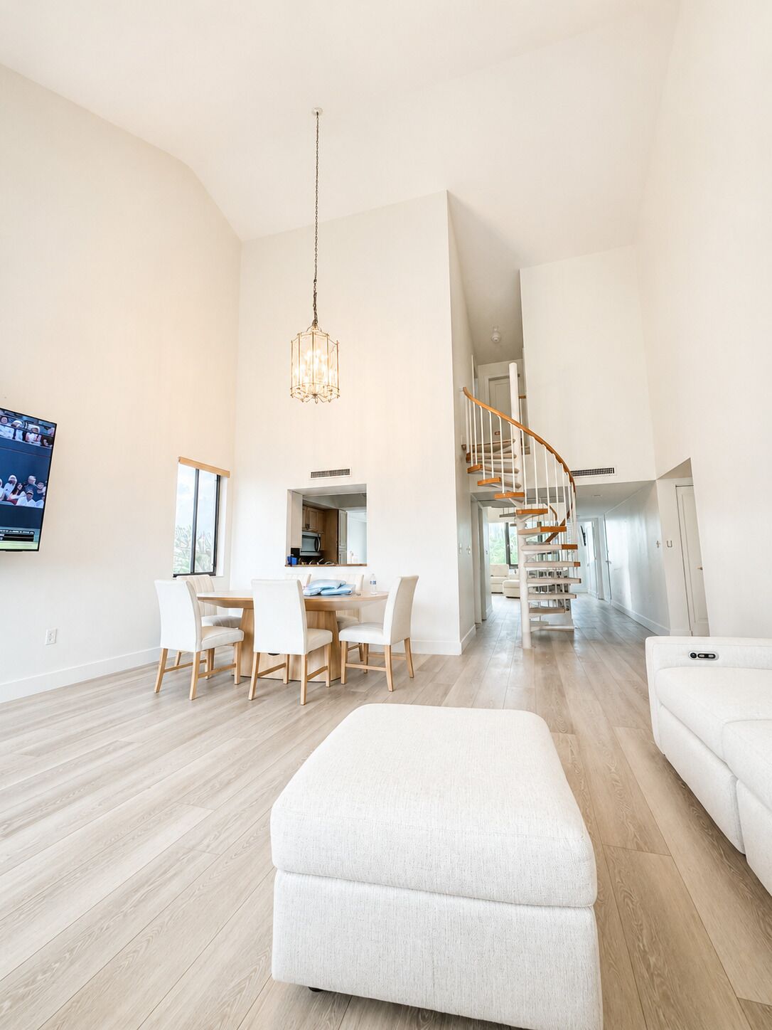 Un vaste espace de vie comprenant une table à manger, des canapés blancs et un escalier menant à un niveau supérieur.