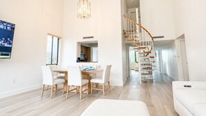 Amplia sala de estar con mesa de comedor, sofás blancos y una escalera que sube a un nivel superior.