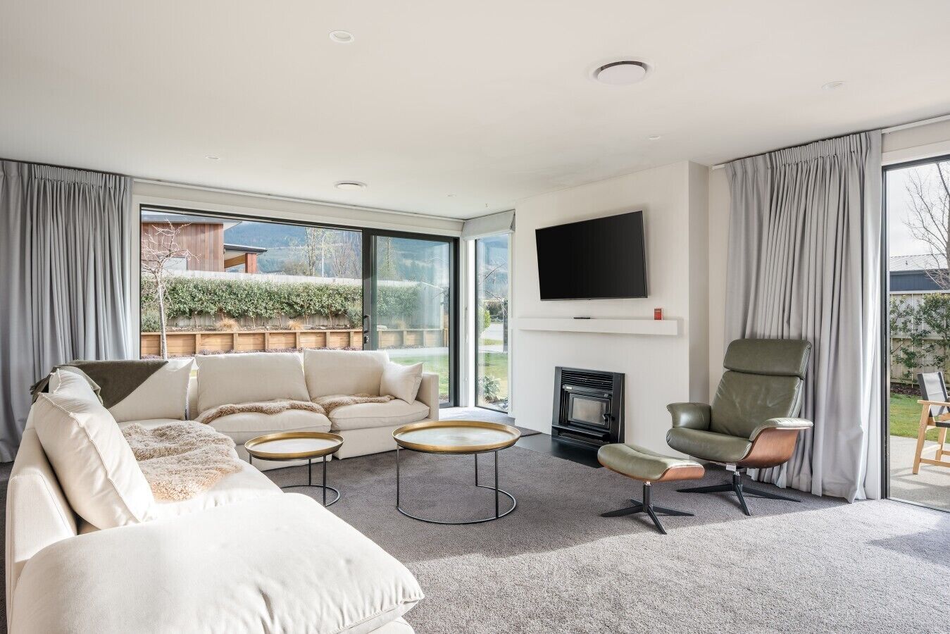 A modern living room with a sectional sofa, a green armchair, a fireplace, and a large TV on the wall.