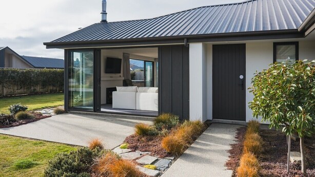 Une maison moderne dotée d’une grande porte vitrée, d’un toit plat et d’un jardin bien entretenu.