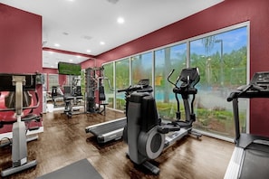 Ein Fitnessstudio mit Cardiogeräten, Gewichtstrainern und großen Fenstern mit Blick auf Grünflächen.