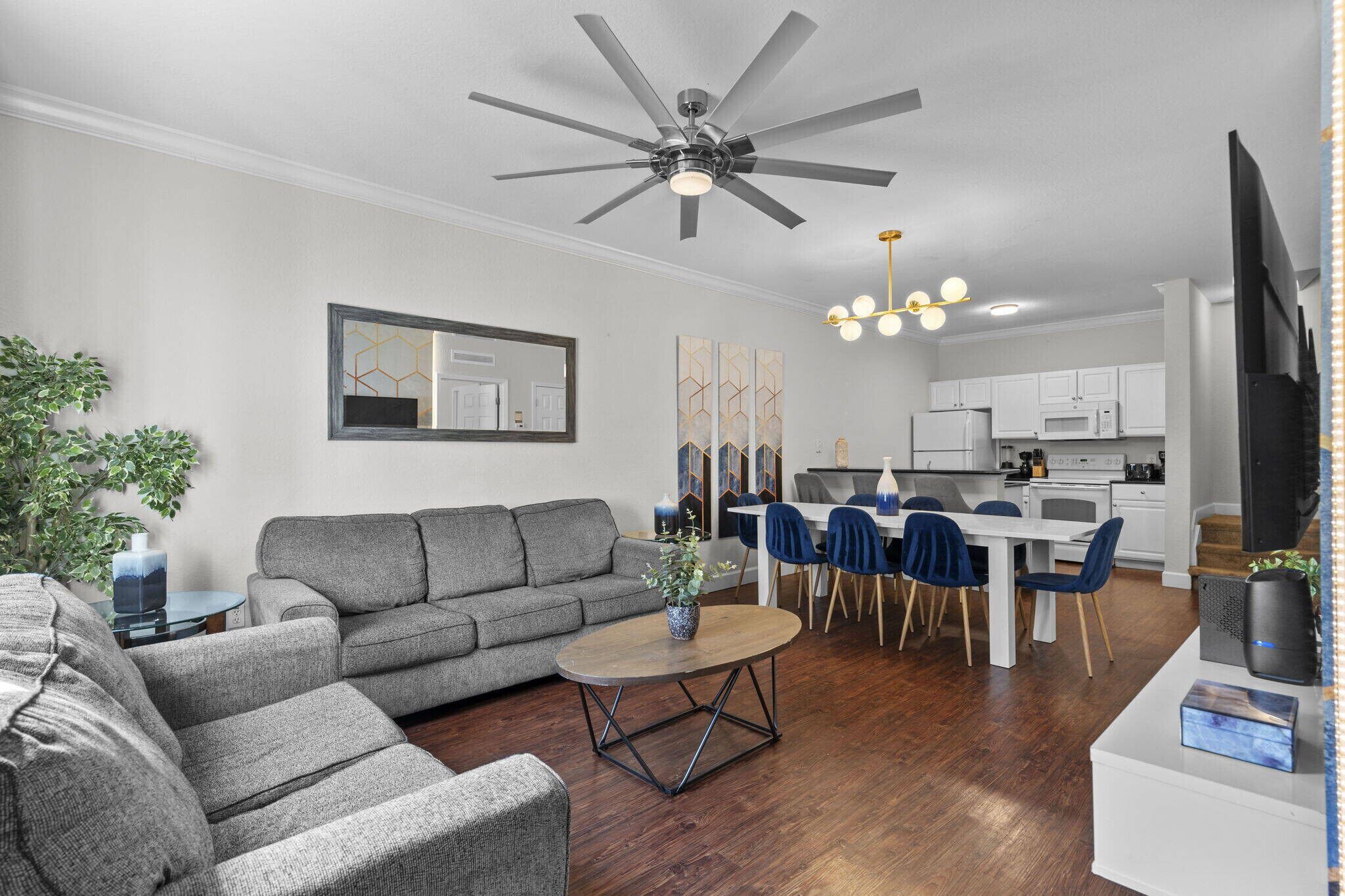 A modern living room with a gray sofa, a coffee table, and a dining area with blue chairs.
