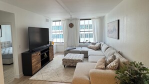 Ein modernes Wohnzimmer mit Flachbildfernseher, Ecksofa, Couchtisch aus Holz und einer Topfpflanze.