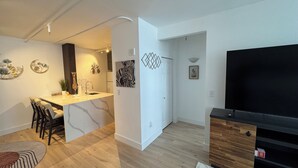 Ein modernes Wohnzimmer mit einem Flachbildfernseher, einem Essbereich mit einer Marmorinsel und einer Küche mit weißen Schränken.