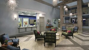 Een ruime lobby met een receptiebalie, meerdere zithoeken en decoratieve wandkunst.