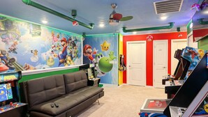 Ein Zimmer mit einer Couch, Spielautomaten und einem Wandgemälde zum Thema Mario.