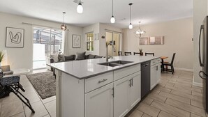Una cocina moderna con una isla central, iluminación colgante y un comedor con mesa y sillas.