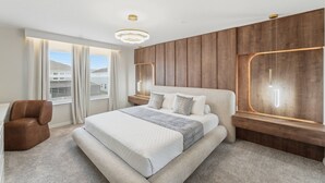 Ein modernes Schlafzimmer mit einem großen Bett, einem Sessel, einem Fenster mit Vorhängen und Holzvertäfelung an den Wänden.