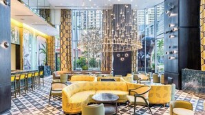 Eine moderne Lounge mit geometrischem Fußbodenmuster, gelben Polstersitzmöbeln und einem zentralen Kronleuchter.