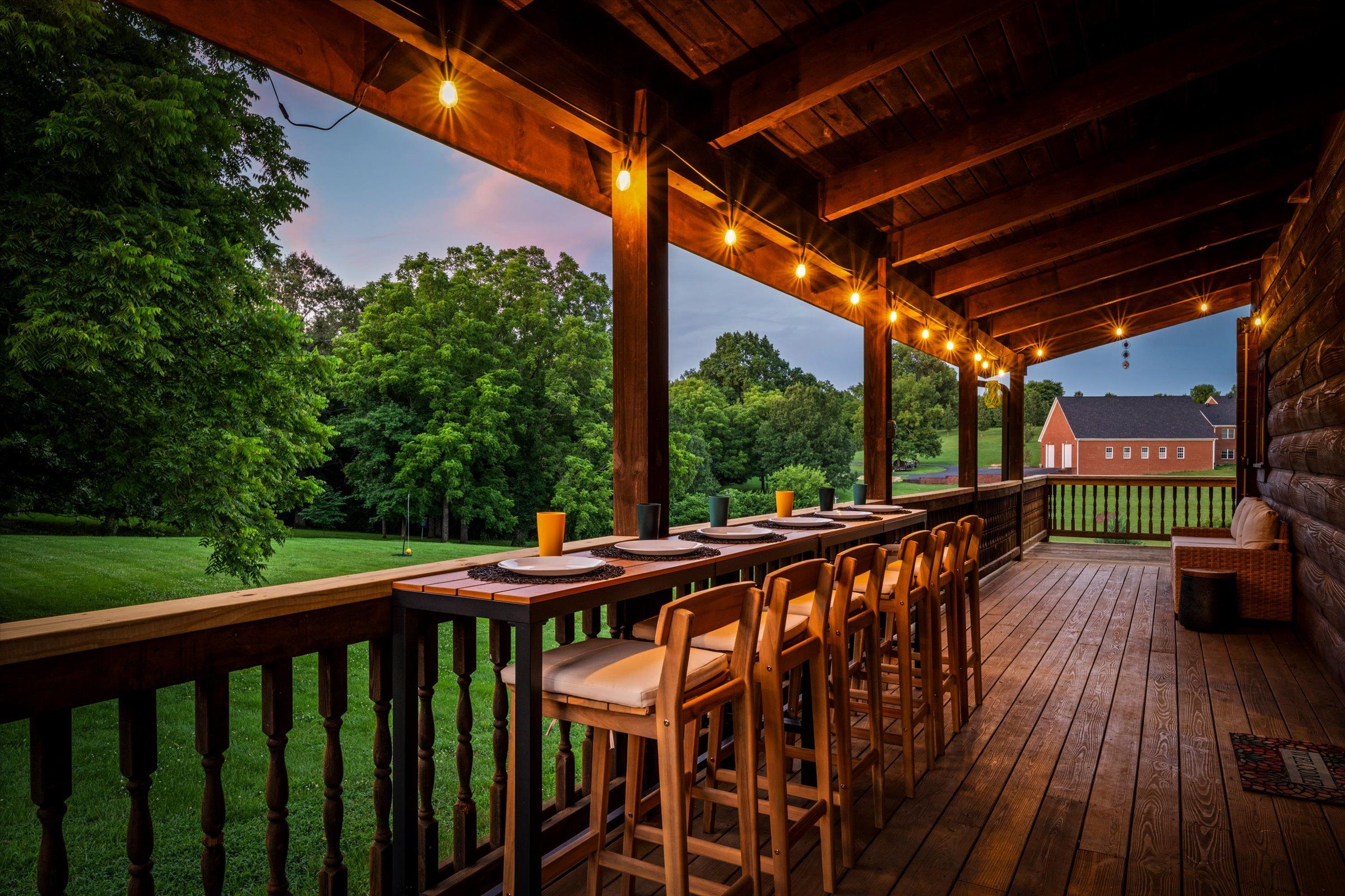 An outdoor deck with a long table set for dining, surrounded by chairs, and a view of a red building in the distance.