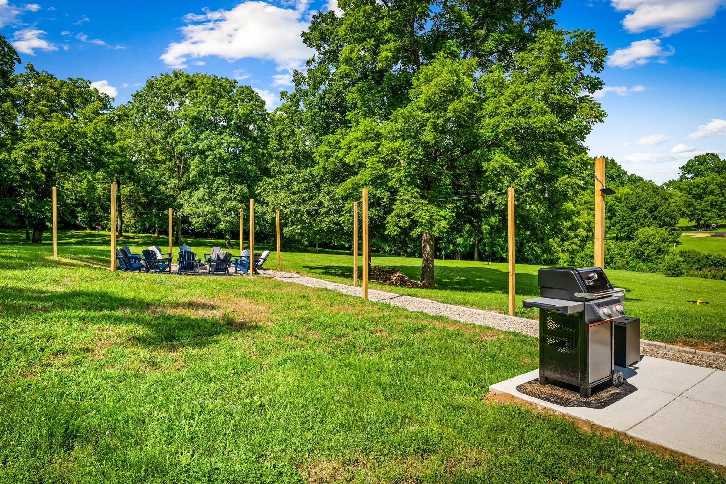 A grassy outdoor area with a barbecue grill, seating area, and trees.