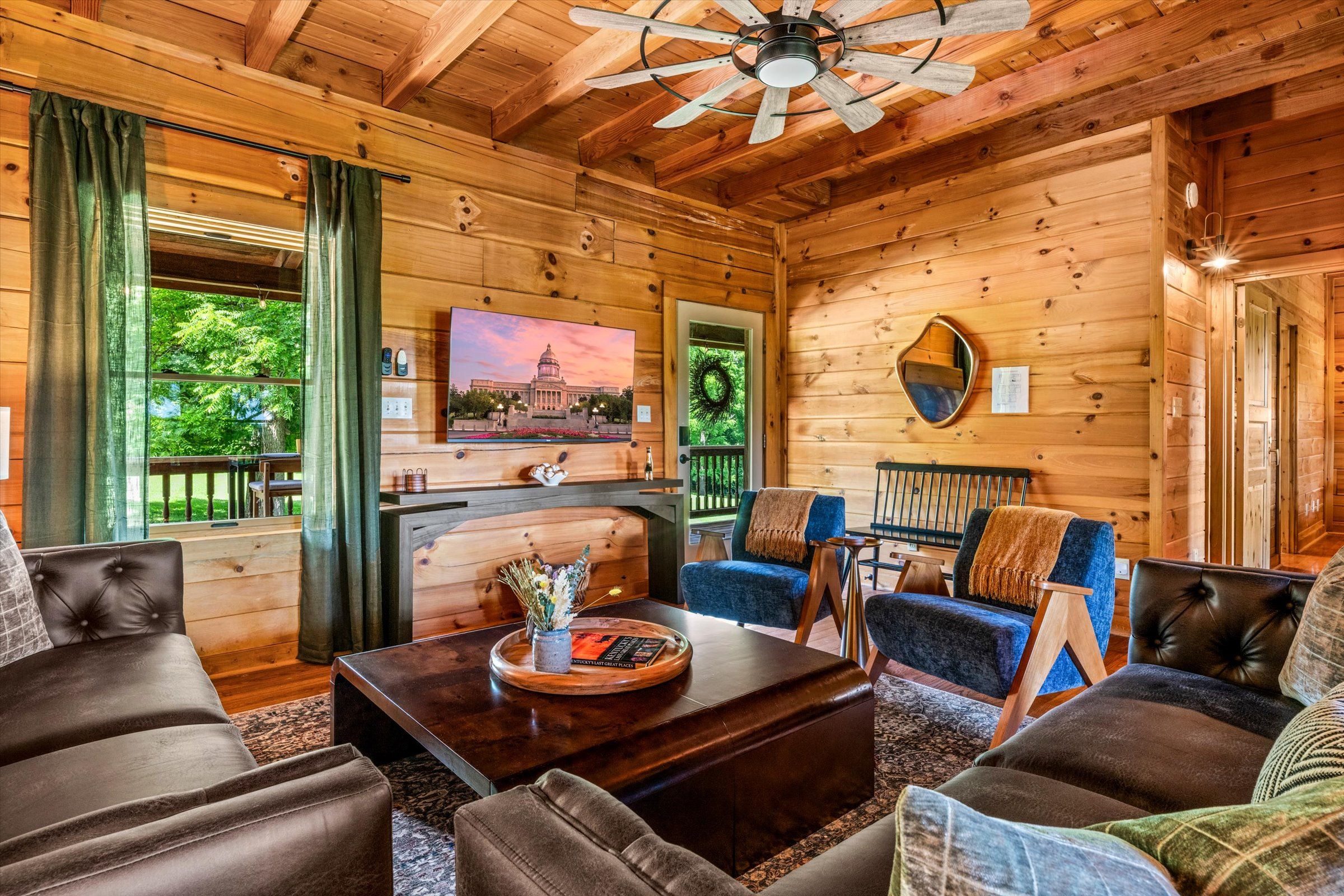 A cozy cabin interior with a fireplace, comfortable seating, and a large window overlooking greenery.