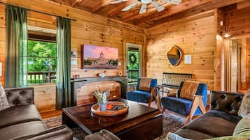 A cozy cabin interior with a fireplace, comfortable seating, and a large window overlooking greenery.