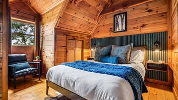 Ein Schlafzimmer einer Holzhütte mit einem Bett, einem Sessel, einem Nachttisch und einem Fenster.
