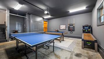 A room with two ping pong tables, a foosball table, and a billiards table.