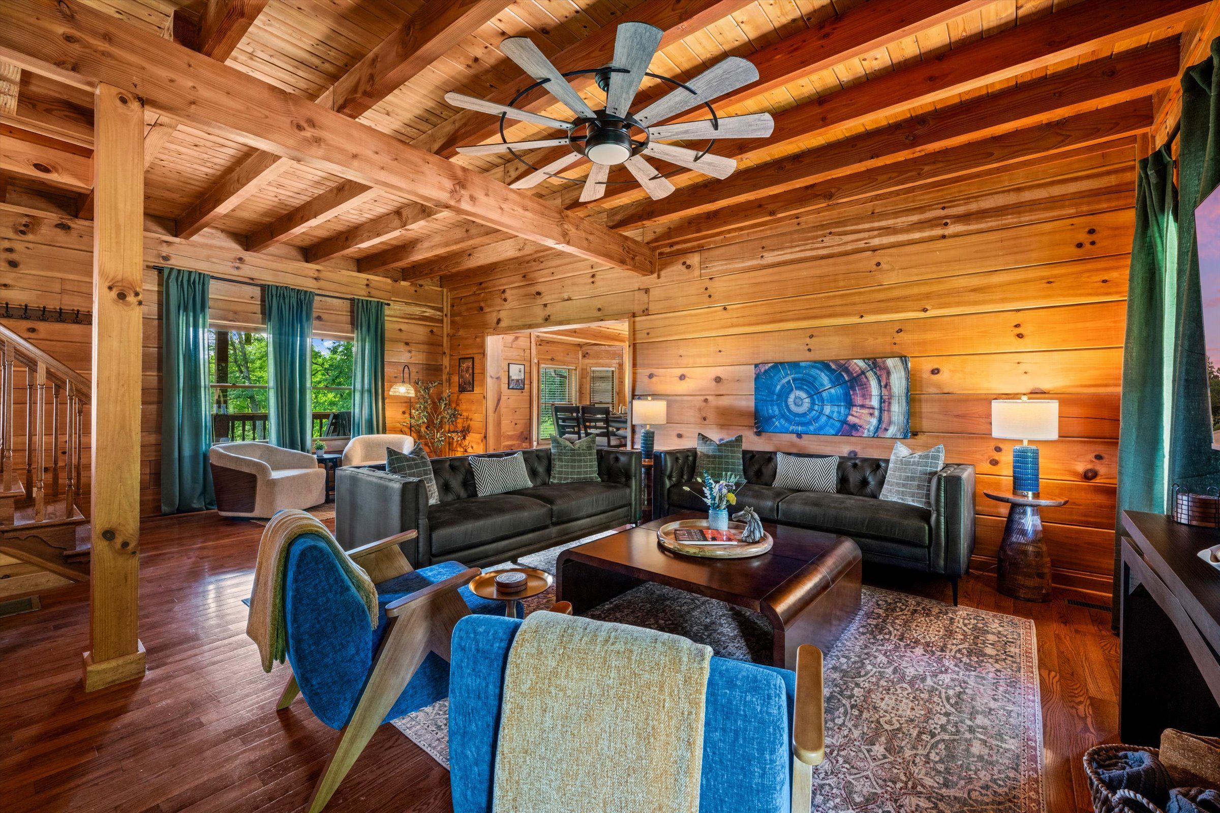 A spacious living room with a high ceiling, wooden beams, a ceiling fan, and a large painting.