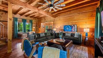 A spacious living room with a high ceiling, wooden beams, a ceiling fan, and a large painting.