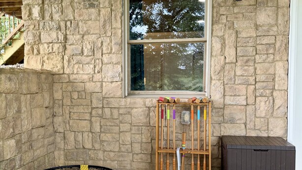 A stone wall, a window, a trampoline, a rack with colorful balls, and a dark storage box.