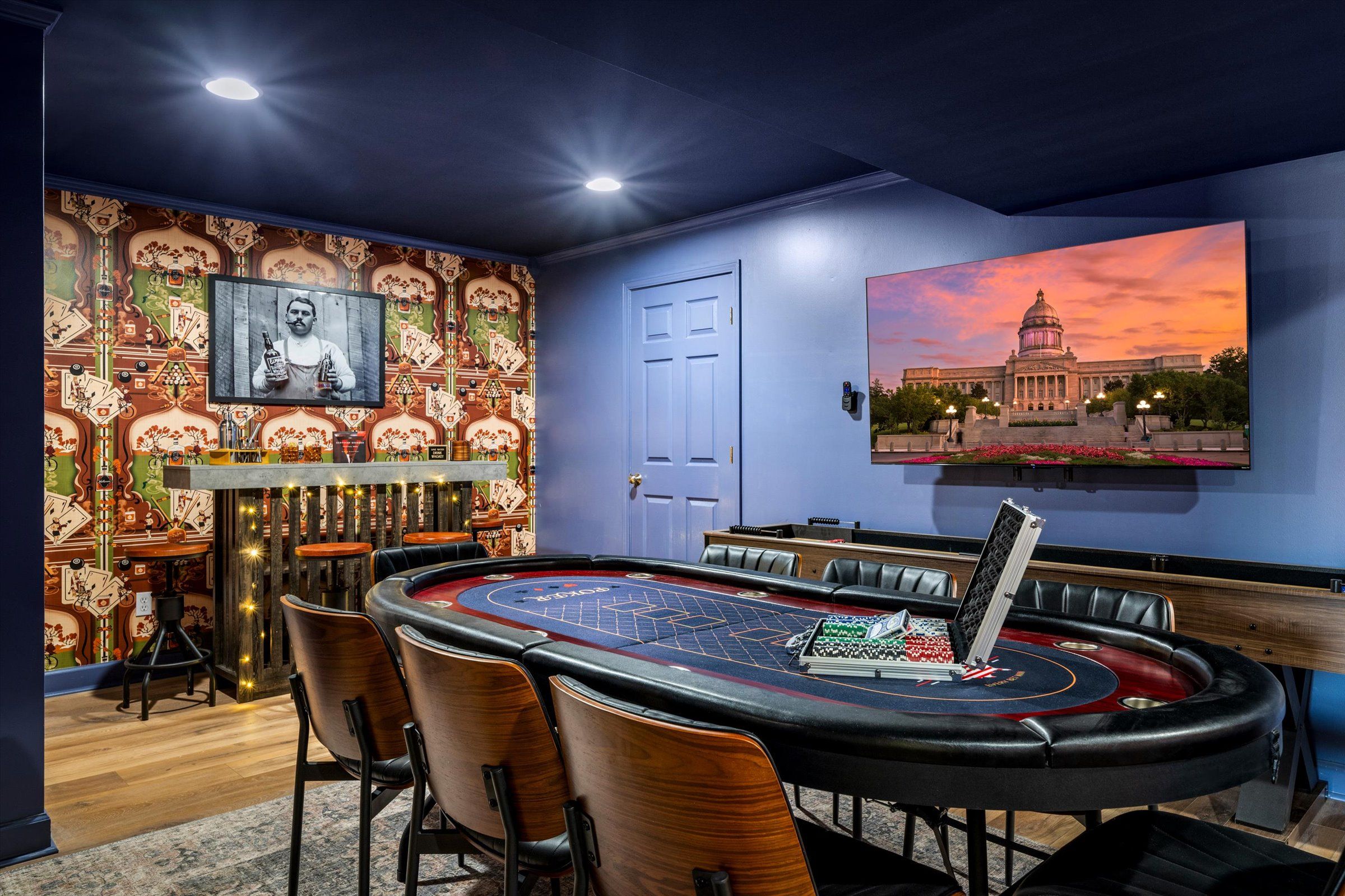 A room with a craps table, chairs, a door, and a wall with a painting of a building.