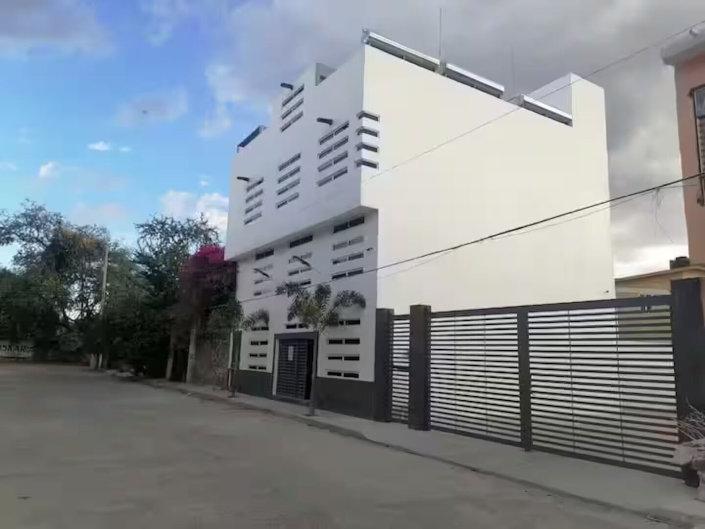 A modern building with a flat roof, multiple windows, and a gated entrance.