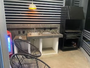 A compact kitchen with a sink, a hanging light fixture, and a black grill.