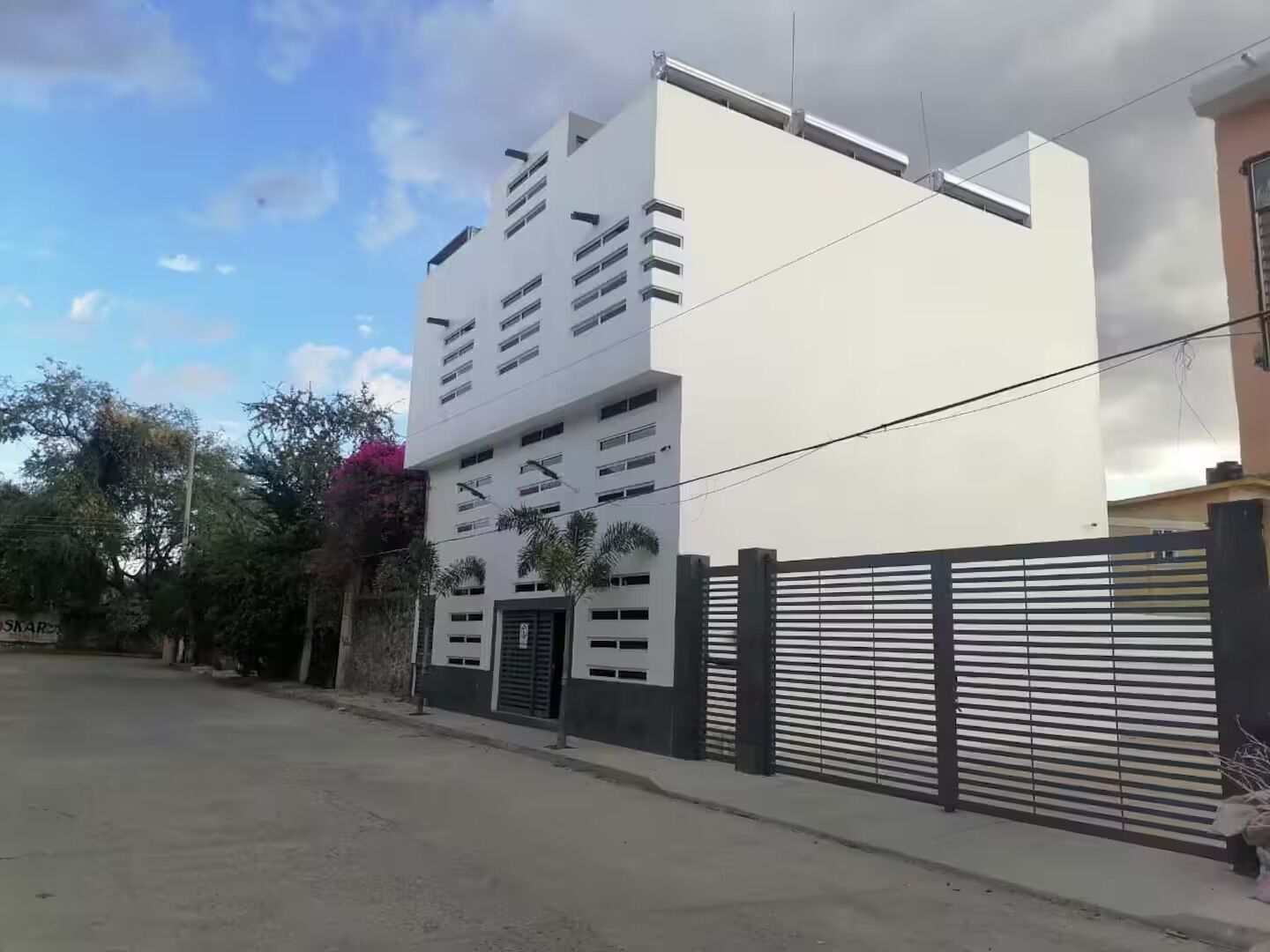 Un immeuble moderne à plusieurs étages, doté d’un toit plat, de grandes fenêtres et d’une entrée sécurisée par un portail.