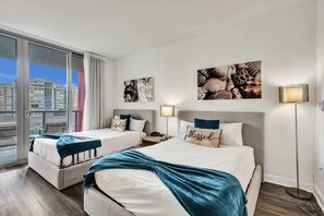 Ein Hotelzimmer mit zwei Betten, einem großen Fenster mit Blick auf Gebäude und Kunstwerken an den Wänden.