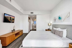 A modern hotel room with a large bed, a wooden console table, a flat-screen TV, and a view of the cityscape. - Inviting Waterfront Stay | Near Ocean & Resort Perks (Hallandale Beach)