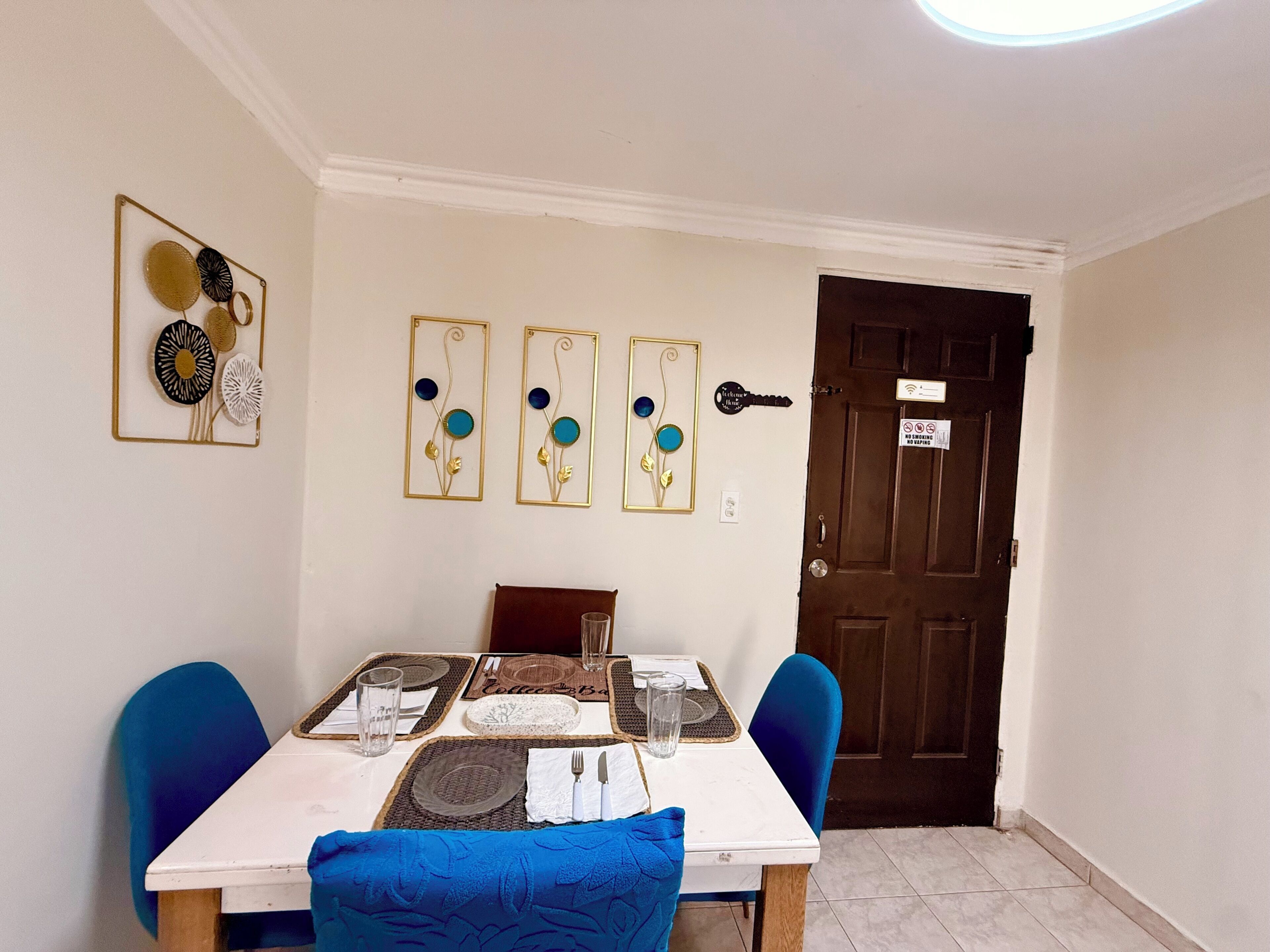 Un coin repas avec une table dressée pour deux personnes, une porte marron avec une pancarte et des œuvres d’art mural.