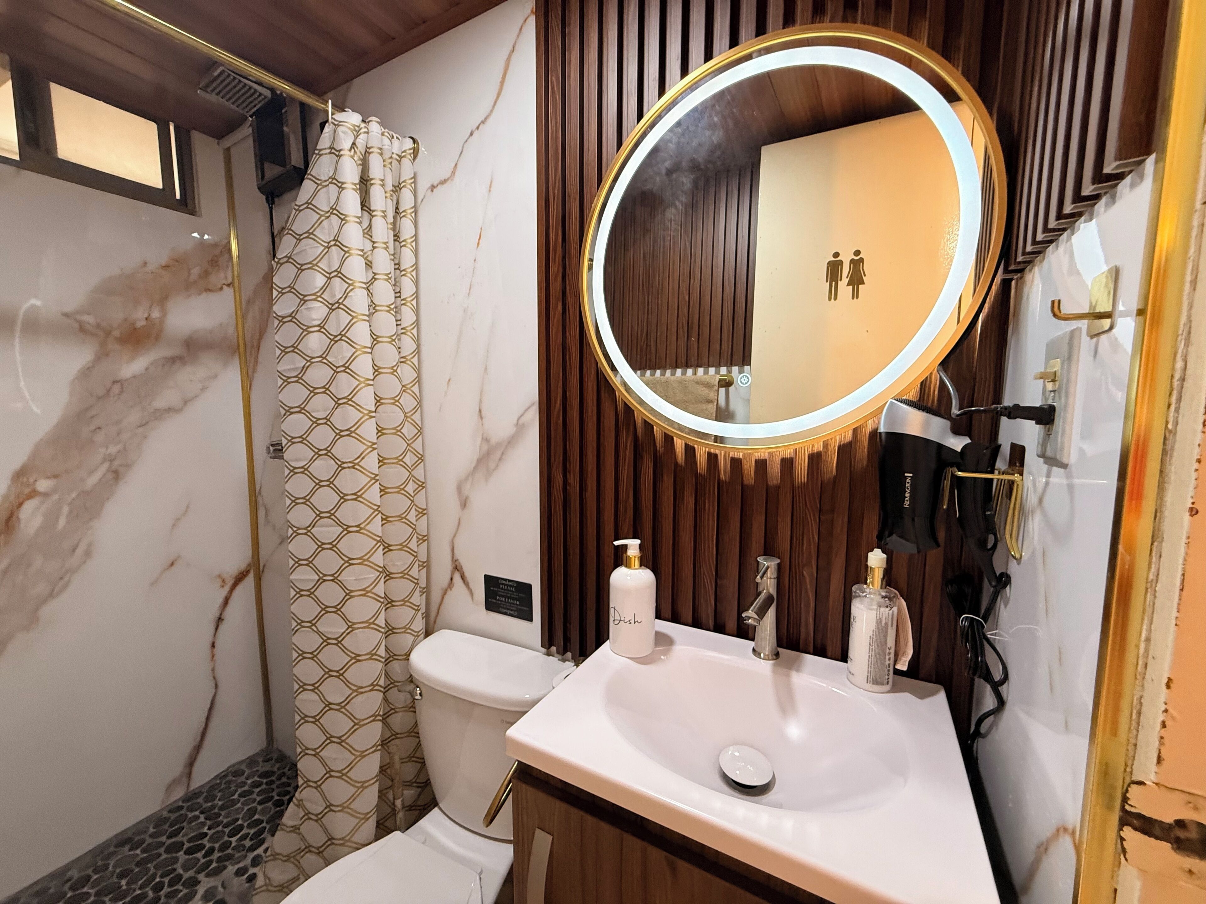 Une salle de bain avec un lavabo blanc, un miroir rond, des toilettes et un rideau de douche à motifs géométriques.