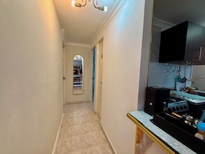 Un pasillo con suelo de baldosas, una puerta que da a una habitación, un espejo y una zona de cocina con estufa y lavabo.