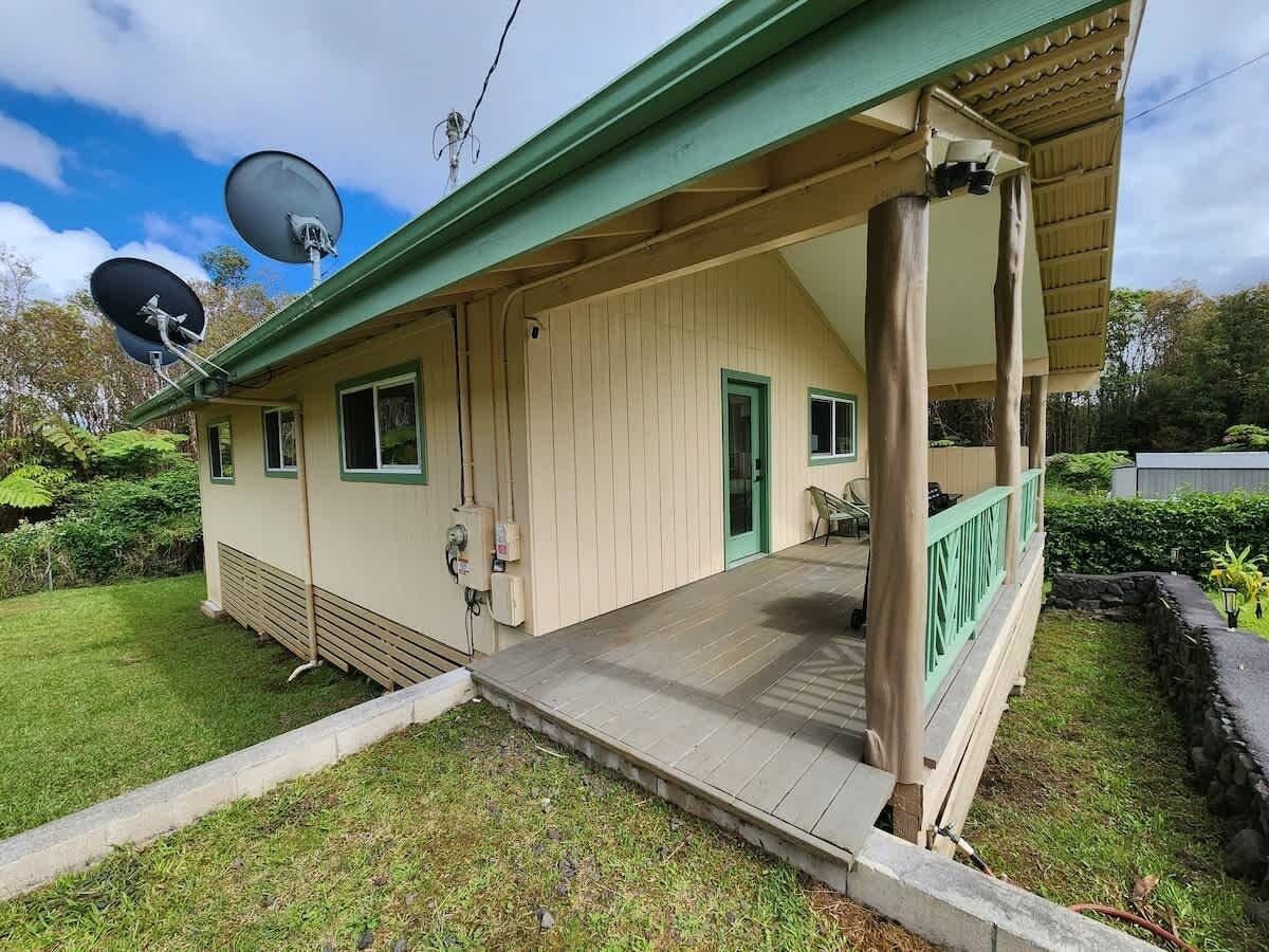 A single-story building with a covered porch, satellite dishes, and a small garden area.