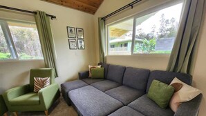 A room with a grey sofa, a green armchair, and a window with curtains. - Hawaii's Trivia Hale an Off the Beaten Path Oasis | AC | Family Friendly (Mountain View)