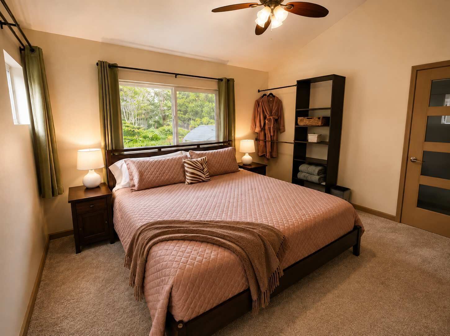 A bedroom with a bed, bedside lamps, a window, a ceiling fan, a wardrobe, and a door.