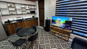 Une cuisine moderne avec des meubles en bois, un coin repas avec une table et des chaises noires, un téléviseur posé sur un meuble en bois et un sol à motifs.