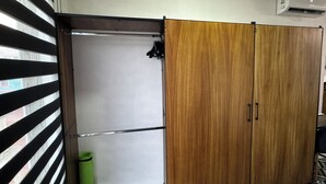 Une pièce avec une armoire en bois à portes coulissantes, une porte blanche, une poubelle verte et un store à rayures.