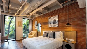 Una habitación de hotel moderna con una cama grande, un escritorio, una silla y vistas a zonas verdes a través de un amplio ventanal.