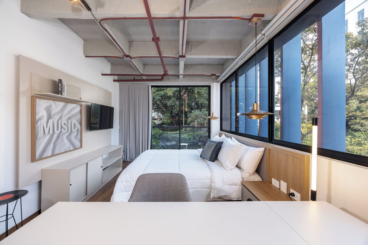 Quarto moderno com uma cama grande, TV na parede e janela com vista para o verde.