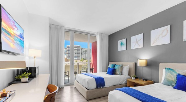 Een hotelkamer met balkon, bureau, stoel, twee bedden en kunstwerken aan de muur.