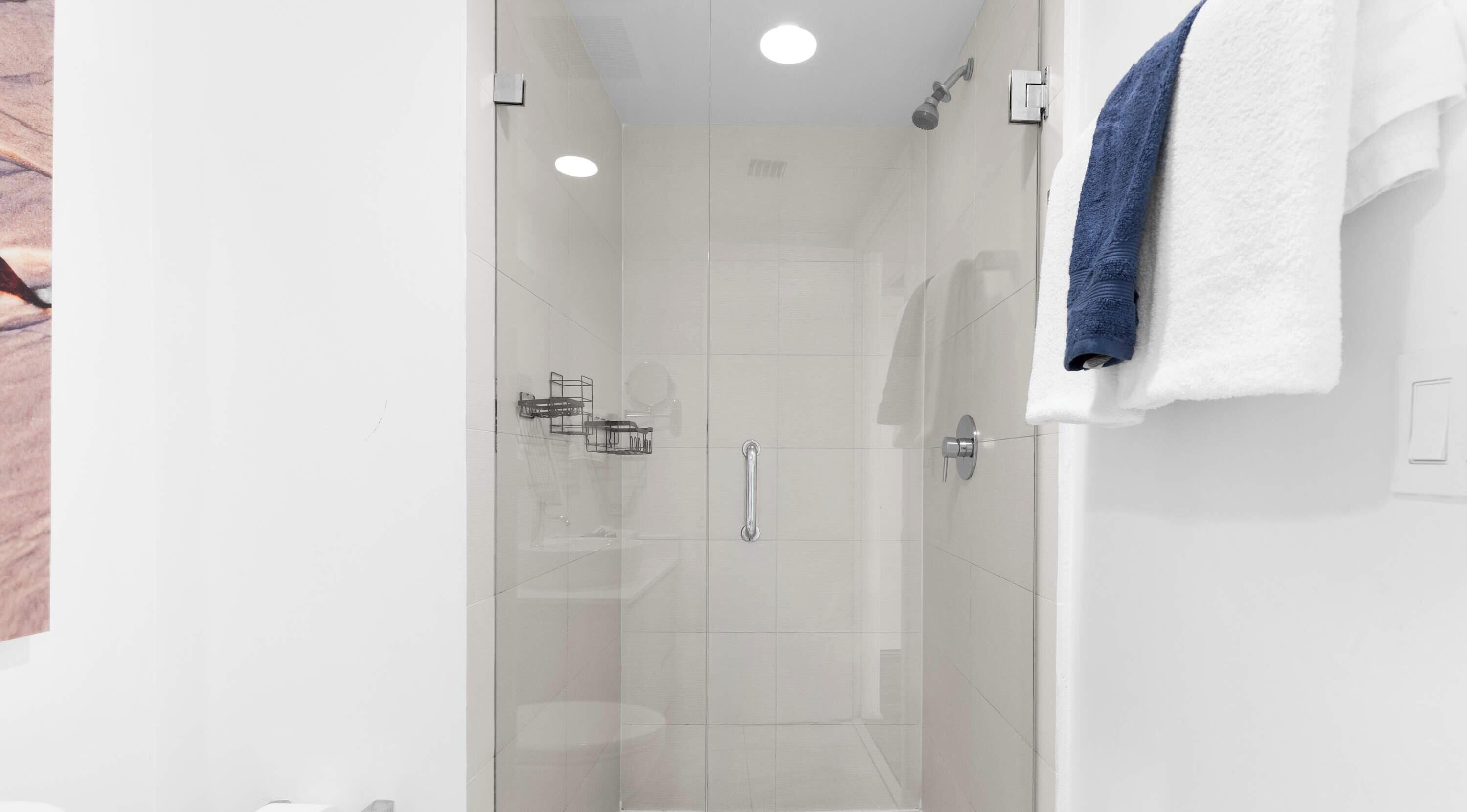 Ein modernes Badezimmer mit Duschkabine aus Glas, einem weißen Handtuch und einer sichtbaren Dusche.