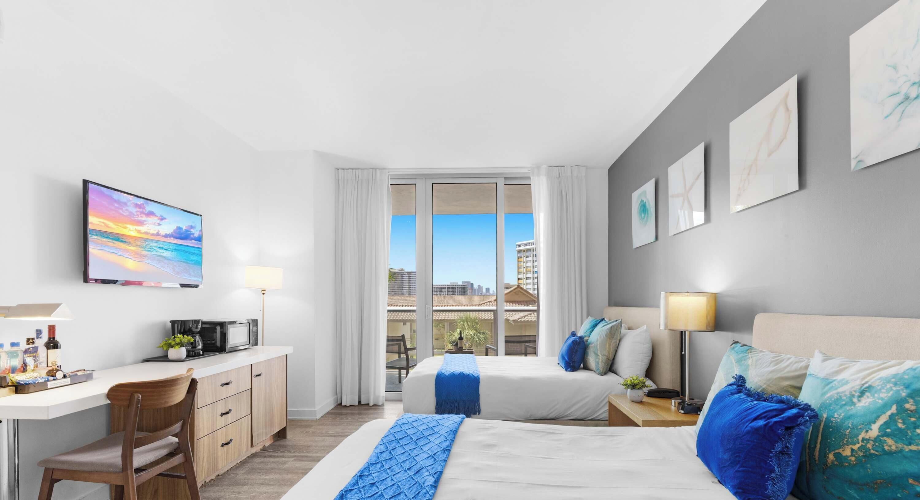 A hotel room with a bed, a desk, a chair, a TV, and a window with a city view.