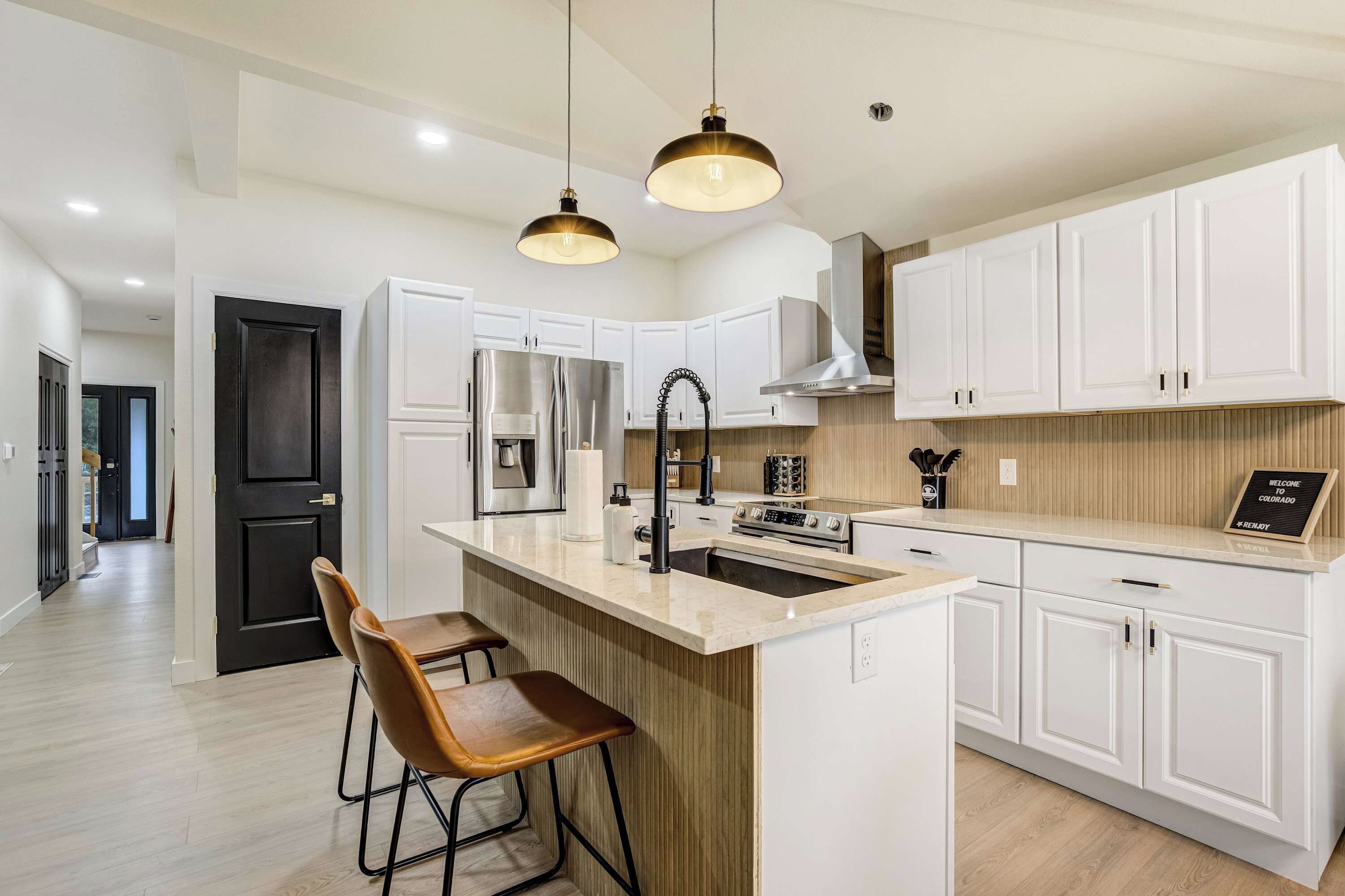 A modern kitchen with white cabinetry, a central island with bar stools, stainless steel appliances, and pendant lighting.