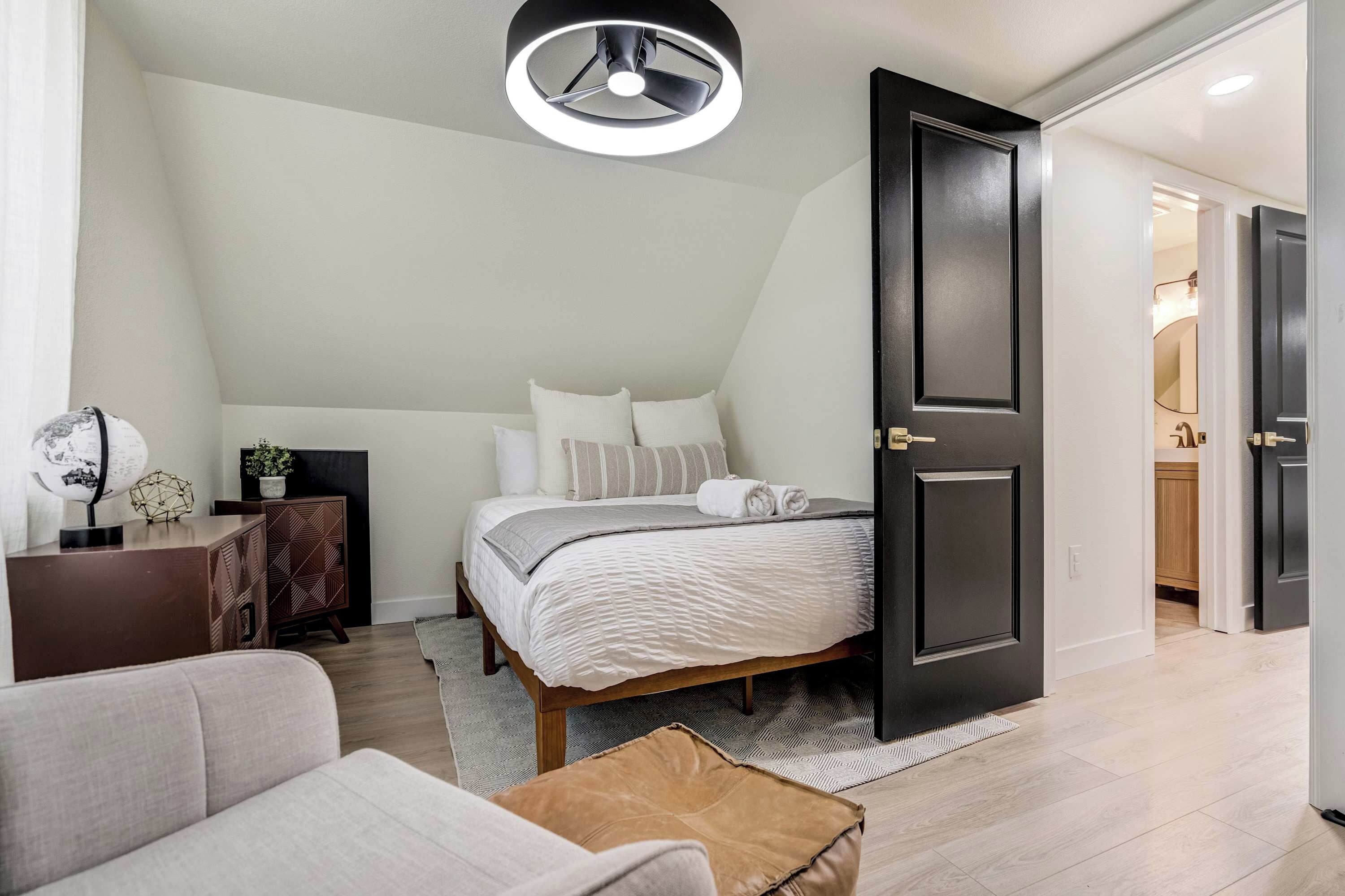 Une chambre à coucher comprenant un lit, une table de chevet, une lampe et une porte donnant sur une salle de bain.