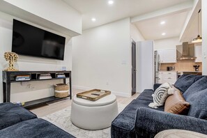 Una sala de estar moderna con un televisor de pantalla plana, un sofá, una mesa de centro y una cocina al fondo.