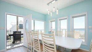 Een eethoek met een witte tafel en stoelen, een barbecue buiten en grote ramen.