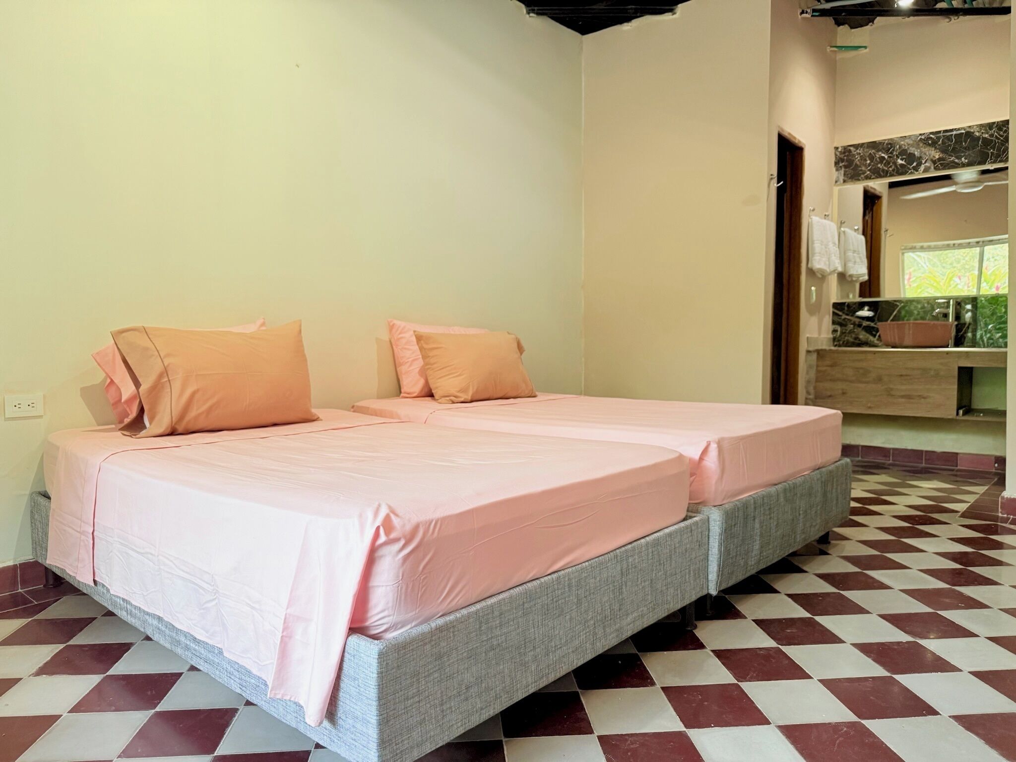 A room with a double bed, a small bedside table, and a bathroom with a mirror and sink.