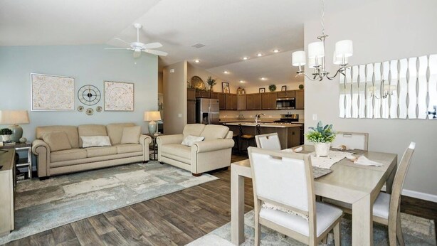 A modern living room with a sofa, a dining table with chairs, a kitchen area with cabinets and appliances, and a ceiling fan. - WELCOME TO YOUR PIECE OF PARADISE (The Villages)