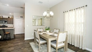 A dining area with a wooden table, chairs, a chandelier, and a view of the kitchen. - WELCOME TO YOUR PIECE OF PARADISE (The Villages)