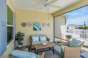 Eine überdachte Veranda mit Deckenventilator, einem Korbsessel, einem kleinen Tisch und einer Topfpflanze.